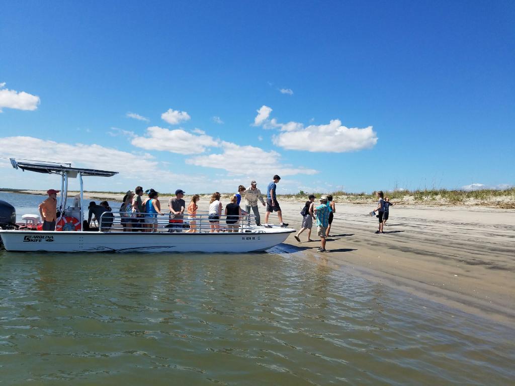 A group of people get off the boat onto Morris Island to explore the beach.