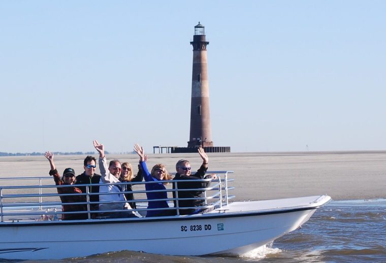 Boat of waving people with Morris Island lighthouse in the background