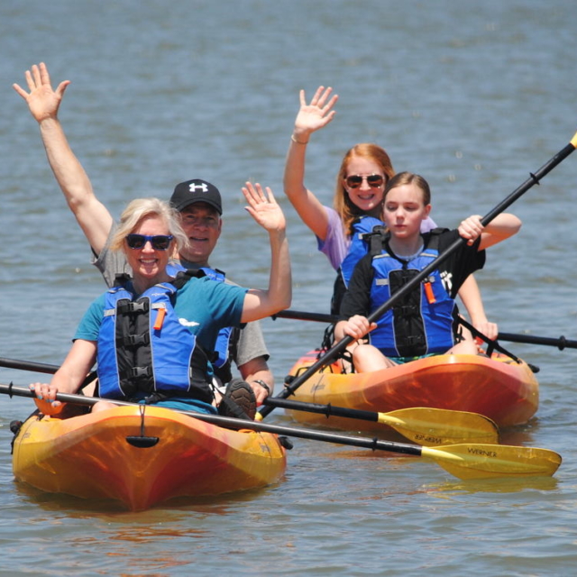 A family waving from the kayaks they rented at COA.
