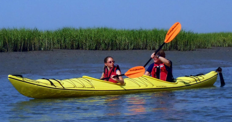 A brother and sister share a tandem kayak and paddle along the lush green waterways.