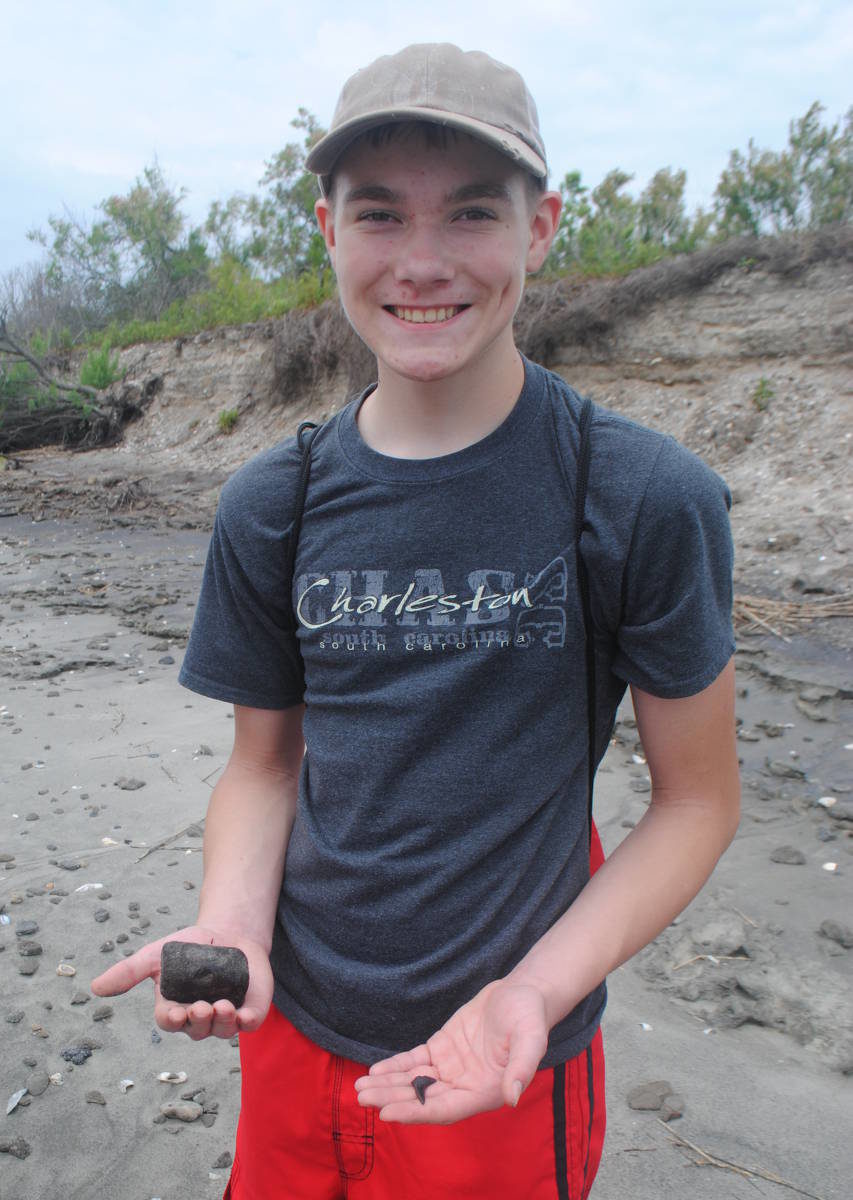 Smiling youth holds an ancient fossil in his open hand on a beach near Charleston, SC.